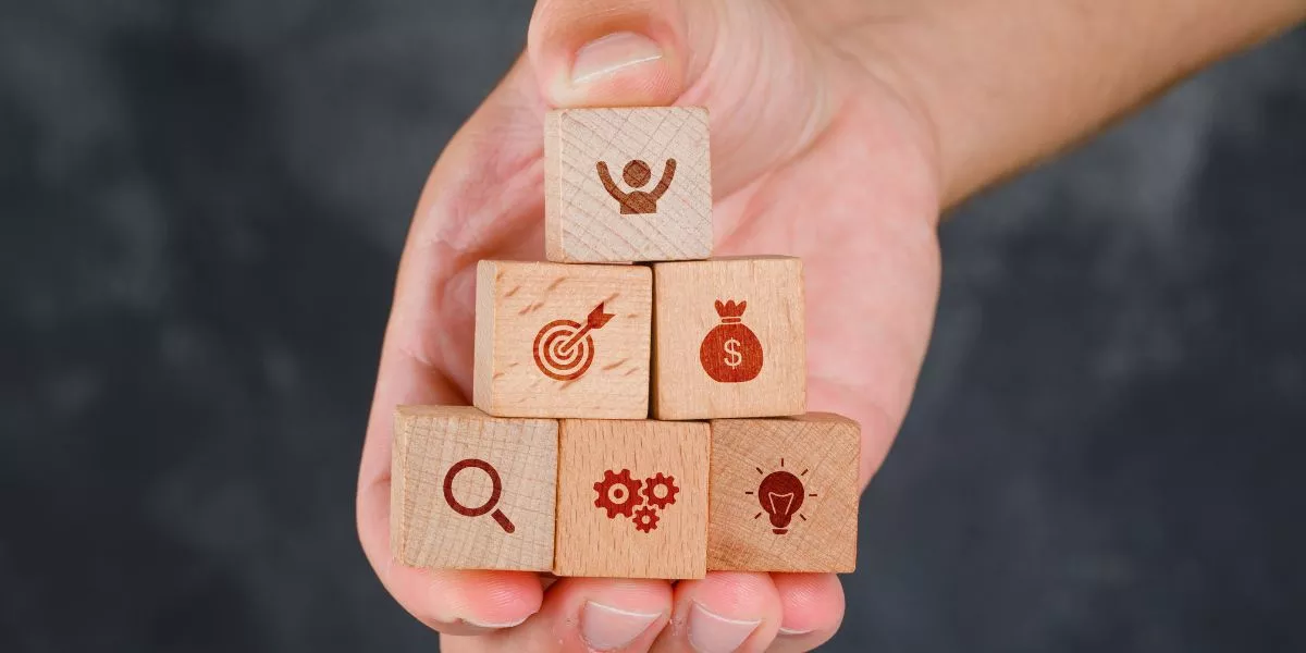 Mano sosteniendo bloques de madera en forma de pirámide con íconos que representan beneficios para empresas y programa de beneficios para empleados.