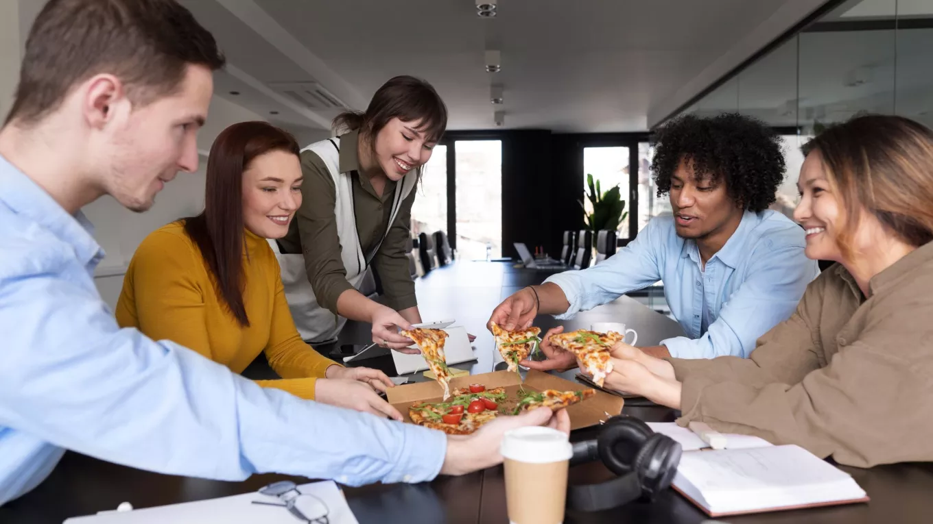 Equipo de trabajo compartiendo una comida en oficina, relacionado con gestión de gastos y reducción de costos de alimentación en una empresa
