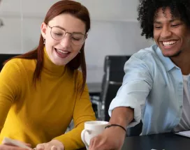 Cuatro personas en la oficina trabajando en conjunto mientras ríen y comparten un café